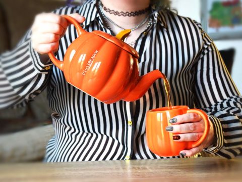 Chrissie is wearing a striped shirt and holding a pumpkin teapot and mug